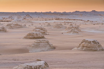 Various chalk rocky formations located on sandy terrain in famous white desert national park against orange cloudless sky in egypt