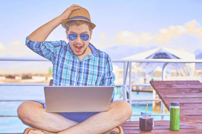 Full length of young man using laptop while sitting outdoors