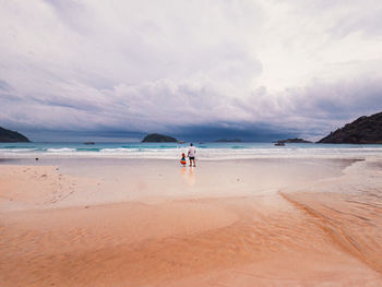 Rear view of woman standing at beach against sky