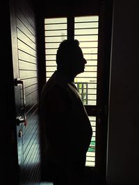 Side view of silhouette man standing against window at home