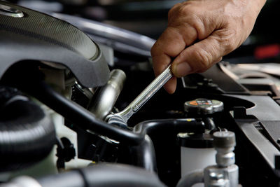 Cropped hand of mechanic repairing car engine with wrench