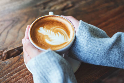 Cropped hand of woman holding coffee cup on table