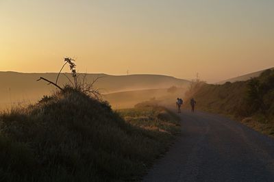 People on road amidst land against sky during sunset