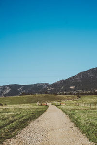 Road amidst field against clear blue sky