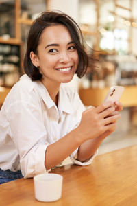 Portrait of young woman using mobile phone at table