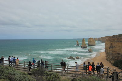 People standing on cliff by sea against sky