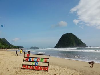 Close-up of text with people at beach against sky
