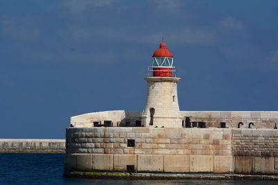 Lighthouse by building against sky