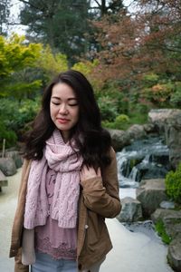 Young woman looking away while standing against trees