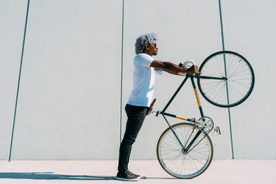 Black and afro man taking the bike and carrying it on a gray background. black cyclist concept.