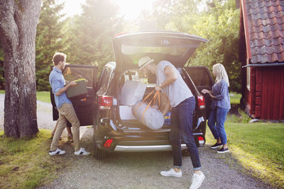 Full length of friends loading luggage into car on road during sunny day