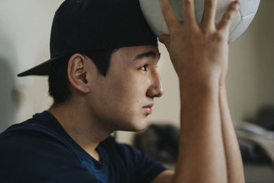 Teenage boy wearing cap and holding sports ball at home