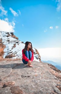 Young woman sitting on rock against sky