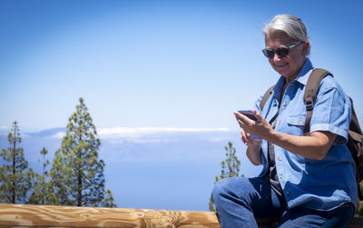 Mid adult man using smart phone against blue sky