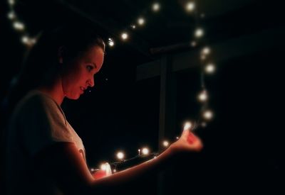 Young woman holding illuminated lighting equipment at night