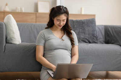 Young woman using mobile phone while sitting on sofa at home