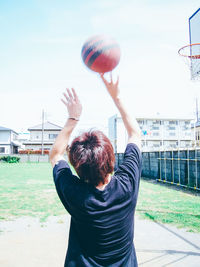 Rear view of young man playing basketball at field against clear sky