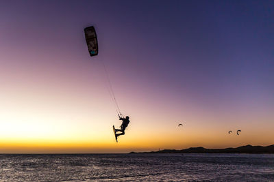 Silhouette person paragliding in sea against sky during sunset