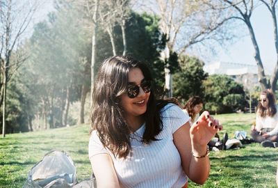 Portrait of smiling young woman with sunglasses against trees