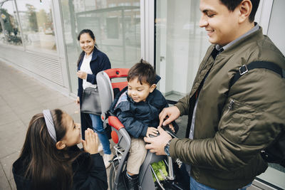 Smiling sister looking at brother sitting on bicycle with parents standing in city