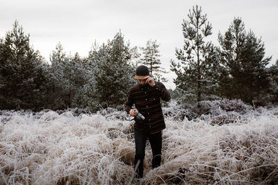 Man with photo camera standing in meadow with frozen grass in winter in scottish highlands