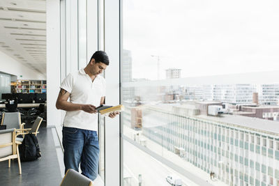 Male university student using digital tablet by window in library