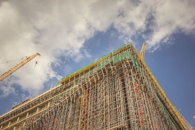 Low angle view of crane by building against sky