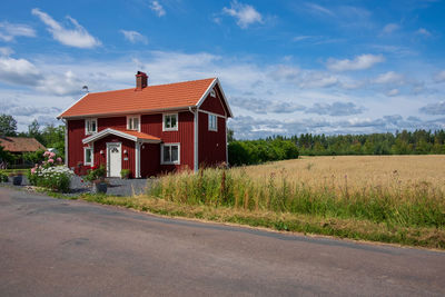 Red house on field by road against sky