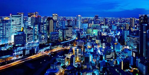 Aerial view of illuminated buildings in city against blue sky