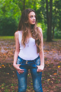 Beautiful young woman looking away while standing against trees