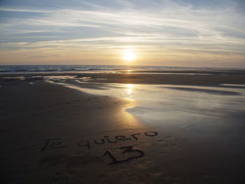 Text on sand at beach against sky during sunset