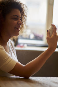 Young woman holding spray bottle at table