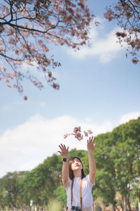 Portrait of happy woman with arms raised against sky