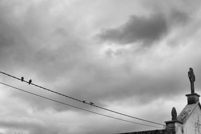 Low angle view of birds perching on statue against cloudy sky