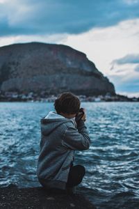 Rear view of boy standing on rock by sea against sky