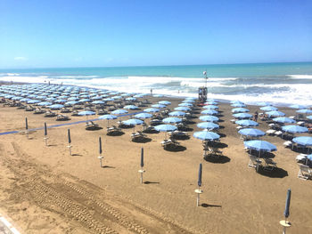 Scenic view of beach with sunshades against clear blue sky