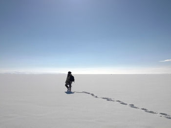 Rear view of man walking on snow covered land against sky