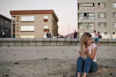 Smiling woman sitting at sandy beach 