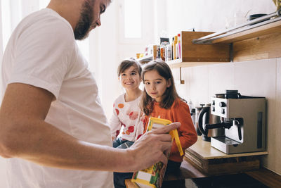Twin siblings looking at father pouring drink in kitchen