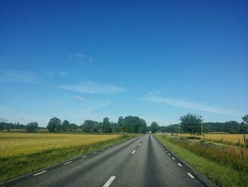 Empty road amidst field against sky