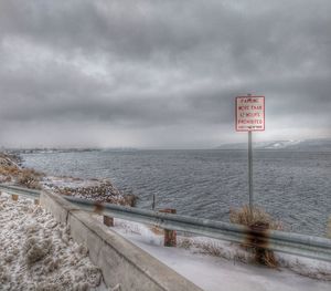 Information sign by sea against sky during winter