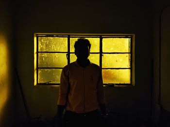 Rear view of silhouette man standing against window