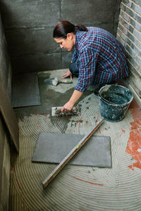 High angle view of mason installing tiles on floor