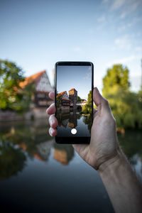 Midsection of person photographing through smart phone against sky