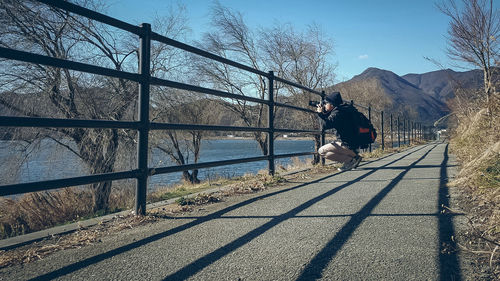 Side view of man photographing while crouching on footpath