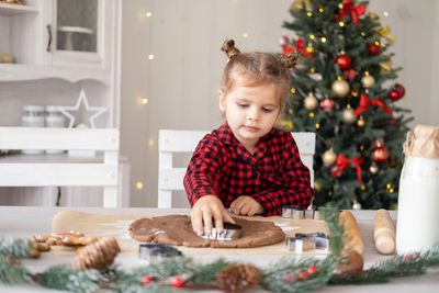Little girl in red pajama cooking festive gingerbread in christmas decorated kitchen
