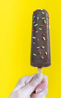 Close-up of hand holding ice cream against yellow background
