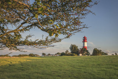 Lighthouse on field by building against sky