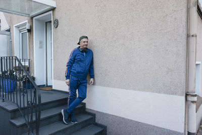 Sportive senior man in tracksuit leaning against house wall