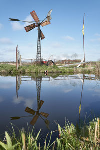 Traditional windmill by lake against sky